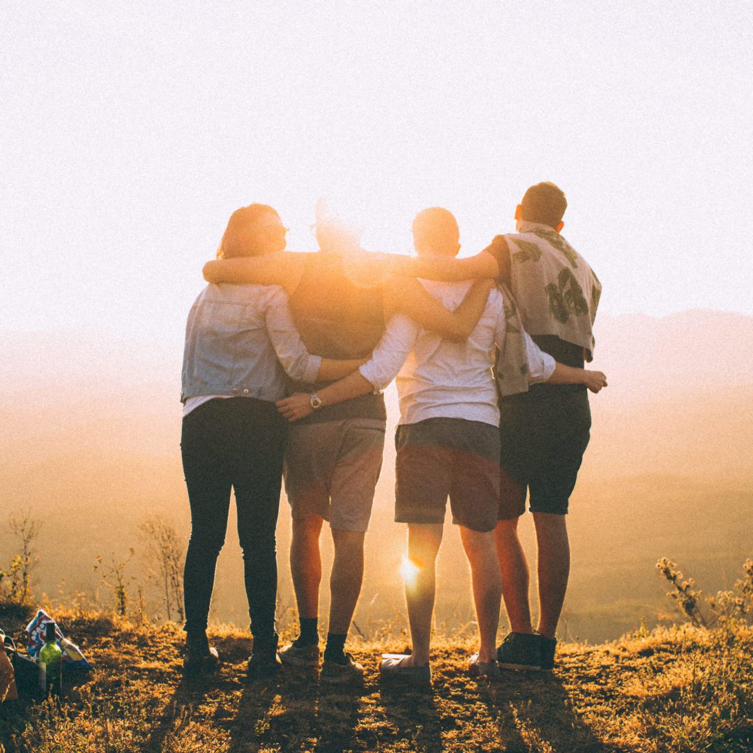 back of group of 3 men and one woman with their arms around each other looking at the sunset Mental Health Resources